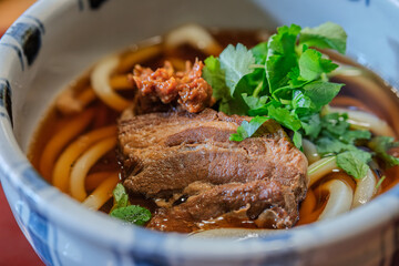 Delicious bowl of Udon Japanese noodle soup with herbs and meat