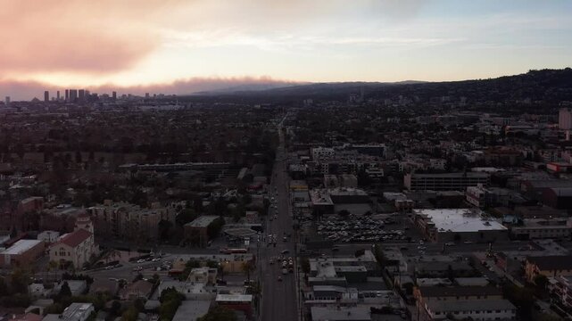Aerial wide rising shot of Melrose Avenue with the Palisades Fire in the distance at sunset in Hollywood, California. 4K