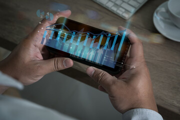 A businessman holds a smartphone, analyzing financial data on a digital screen with charts and graphs, using technology for online trading, marketing, and investment success.
