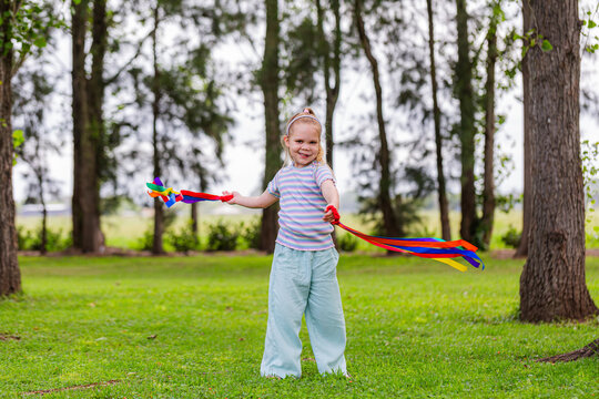 Girl with rainbow streamers running around outside in country with colourful streamers