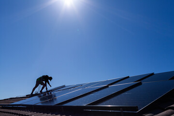 Tradesman laying solar panel on roof under blue sky during solar power system installation job