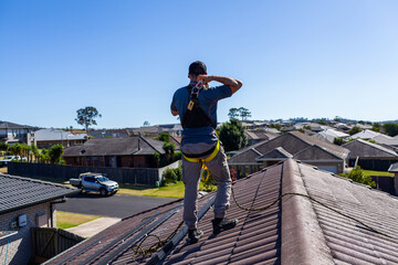 Tradesman climbing on roof of house clipping safety harness to rope for safety compliance