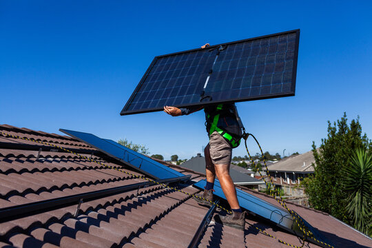 bifacial solar panels being carried on rooftop during solar system installation by electrician