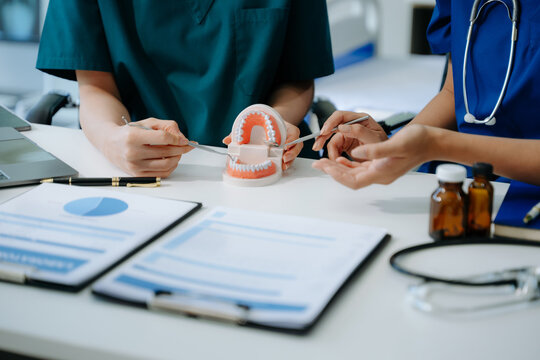 Concentrated dentist sitting at table with jaw samples tooth model and working with tablet and laptop in dental office