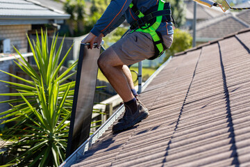 Tradesman electrician lifting black bi-facial solar panels onto roof ready for installation