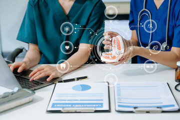 Dentist sitting at table with jaw samples tooth model and working with tablet and laptop in dental...