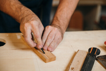 Close-up of carpenter hands using a chisel to mark and shape a wooden plank in a workshop. Hands expertly handling the chisel, demonstrating precision and dedication to craftsmanship in woodworking