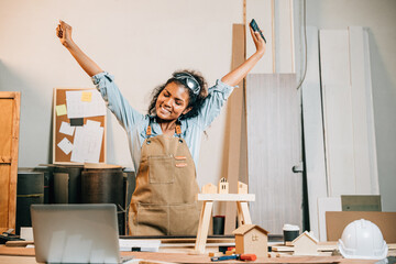 Joyful carpenter woman raises her arms in celebration, expressing excitement in the workshop,...
