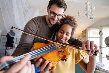 Music is so much fun. Young father teaching his little daughter to play violin and smiling.