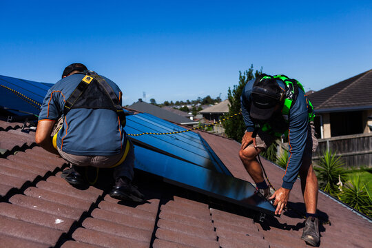 Tradesman electrician and apprentice installing solar panel system on rooftop in Australia