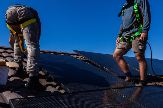 Tradesman electrician and apprentice installing solar panel system on rooftop in Australia