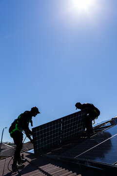 Tradesman electrician and apprentice installing solar panel system on rooftop in Australia