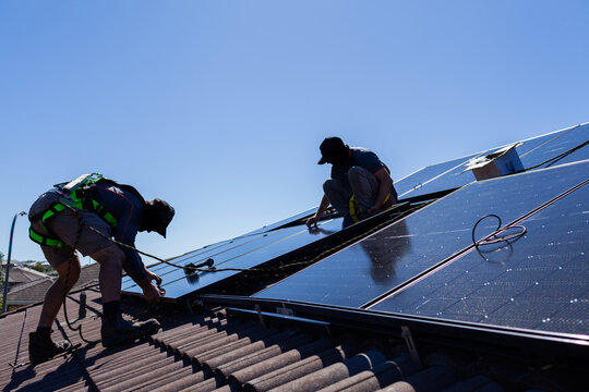 Tradesman electrician and apprentice installing solar panel system on rooftop in Australia