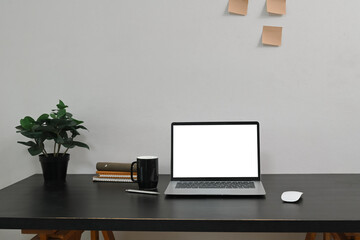 Modern workstation with blank laptop screen, notebooks, and a green plant