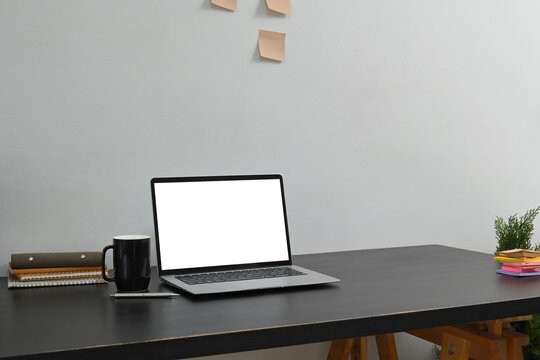 Laptop with a blank screen, a coffee mug, and stationery on black wooden desk