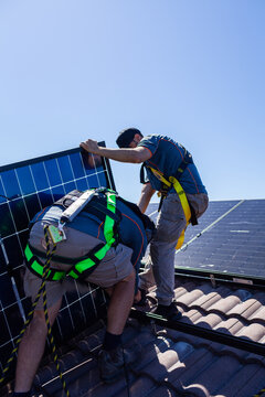 Tradesman electrician and apprentice installing solar panel system on rooftop in Australia