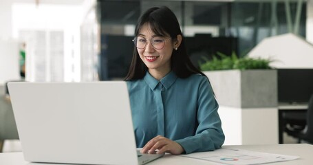Positive young Asian manager woman in stylish glasses typing on laptop computer at workplace, smiling, using online communication for good job result, analyzing successful marketing business strategy - Powered by Adobe