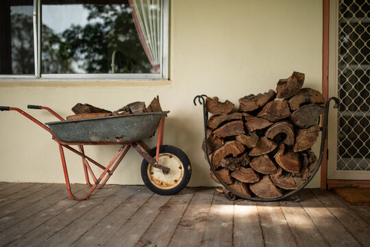 Wheelbarrow and stack of wood on verandah of country home ready for winter