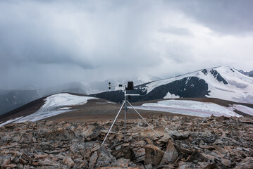 Automatic meteorological station on stone hill with view to large snow-capped mountain range....