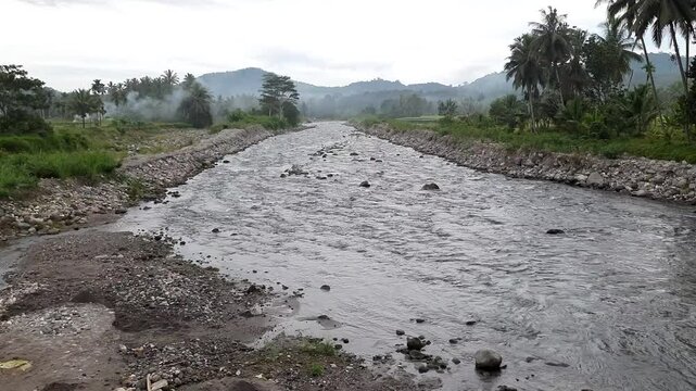 Scenic view of the Batang Anai River in Kayu Tanam, Padang Pariaman, West Sumatra, Indonesia, at dawn. Clear water, rocky riverbanks, and lush greenery