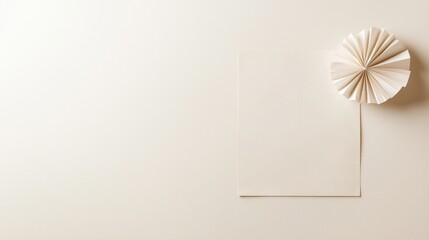Minimalist paper artwork on a beige background, featuring a folded paper rosette and blank card.