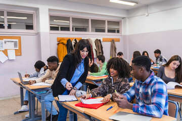 High school teacher helping students studying together in classroom