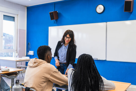 High school teacher helping students using laptop in classroom