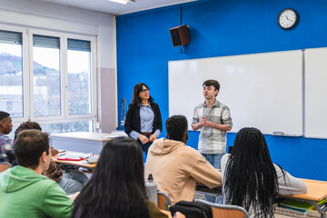 High school students presenting project in classroom with teacher supervising