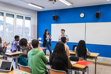 High school students applauding classmate and teacher in modern classroom