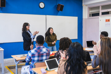 High school students applauding classmate after presentation in modern classroom