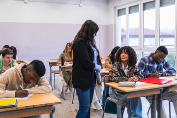 High school teacher helping students during exam in classroom