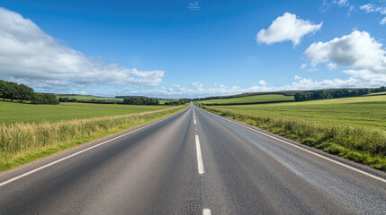 Fototapeta premium Wide road into distance, flanked by green fields and blue sky. High-definition, horizontal composition. Serene beauty.