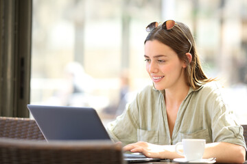 Happy woman using laptop sitting in a bar