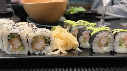 Close-up shot of a platter featuring two types of sushi rolls. The platter rests on a dark rectangular plate. Japanese cuisine, seafood, and healthy eating concept.