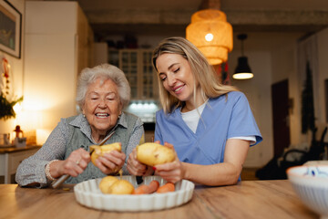 Portrait of elderly companion assistant and senior woman peeling potatoes. Home health care...
