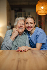 Portrait of caring healthcare worker visiting a senior patient at home, hugging her.