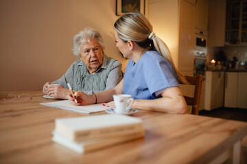 Social worker helping elderly lady with managing her finances, working on financial plan.