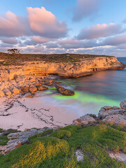 Coastal cliffs glow in the warm light of sunset highlighting a hidden beach with clear turquoise water.