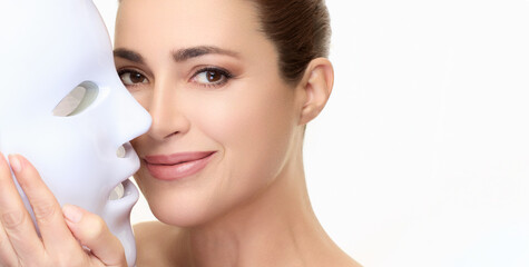 Woman smiling while holding LED facial mask for beauty and skincare treatment with photon therapy...