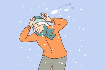 Happy woman plays snowball and dodges snow flying at head, rejoicing in arrival of winter days