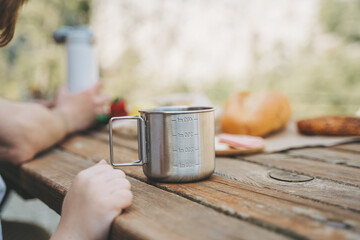 School boy kid child having a family picnic and looking at coffee, tea metallic mug that stands on a wooden table with bread and vegetables.