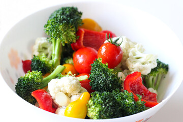 Vibrant fresh vegetable salad with broccoli, cherry tomatoes, bell peppers, and cauliflower in a white bowl. Healthy eating concept