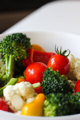 Vibrant fresh vegetable salad with broccoli, cherry tomatoes, bell peppers, and cauliflower in a white bowl. Healthy eating concept