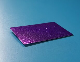 A shiny purple glitter card reflecting light, resting on a vibrant blue surface.