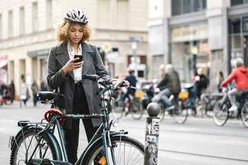 Woman with bicycle and smartphone in the city, Berlin, Germany