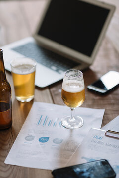 Beer bottle, glasses, documents and laptop on table