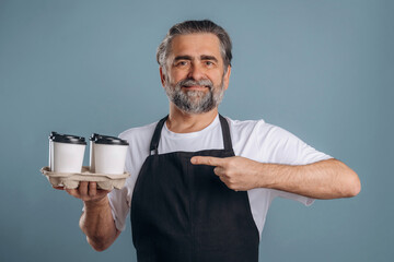 Fresh drinks in hands of a waiter. Senior man is standing in the studio against background