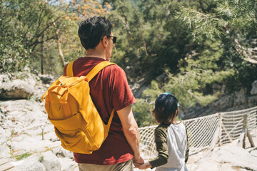 Close-up rear view of tourists school boy and his dad walking a stone footpath in spring forest. Child boy and father wearing casual clothes and yellow backpack while hiking in summer greenwood forest