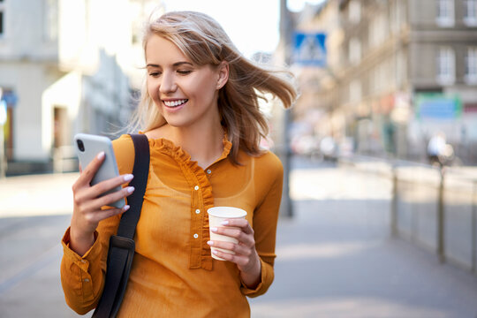 Smiling young woman with smartphone and takeaway coffee in the city