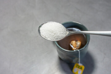Spoonful of sugar above a hot cup of tea